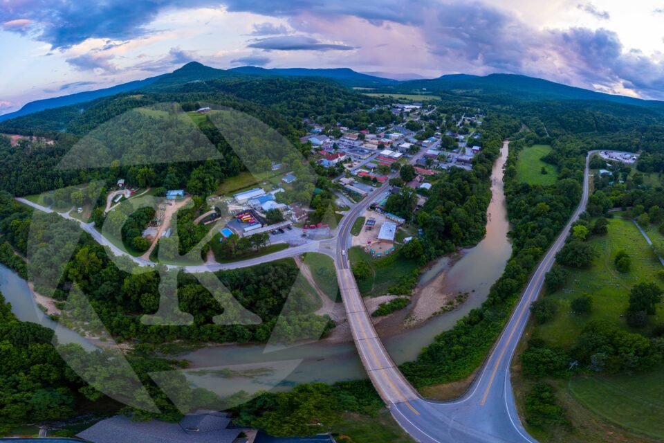 Aerial shot of roads going in and out of a town, surrounded by trees and mountains